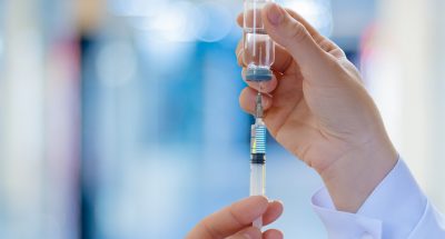 The doctor fills a syringe with vaccine on blurred background.