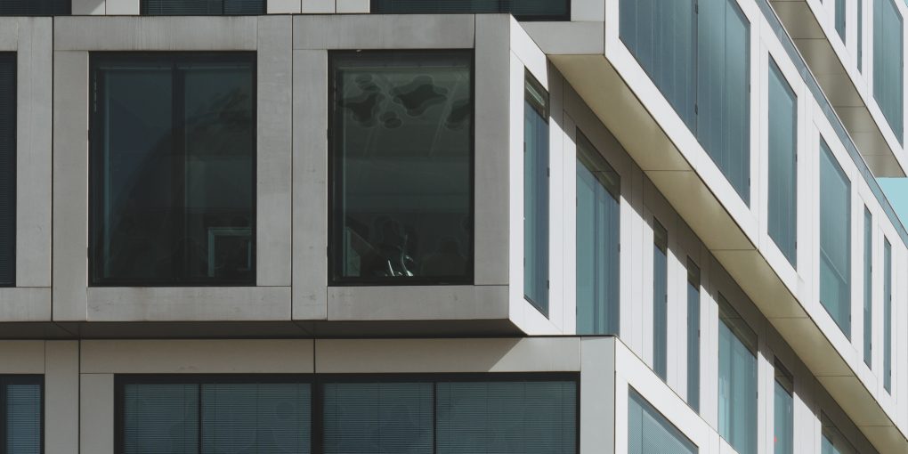 A vertical shot of a grey concrete building with big windows under the blue sky