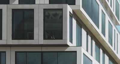 A vertical shot of a grey concrete building with big windows under the blue sky