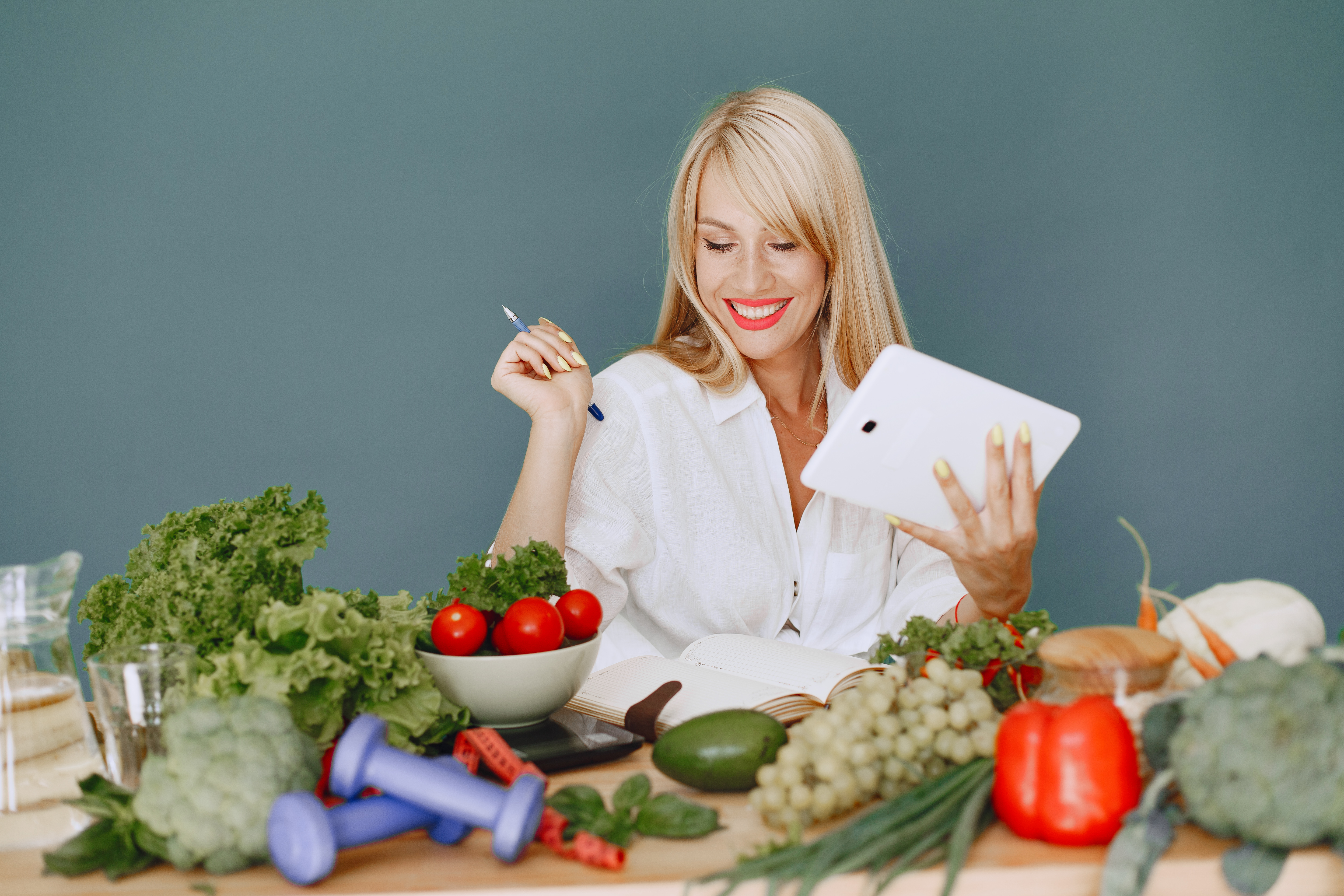 Beautiful girl make a salad. Sporty blonde in a kitchen. Woman writing recipe in notebook.