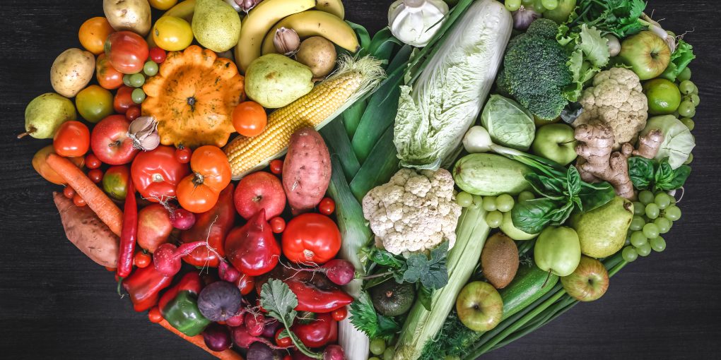 Heart made of fresh vegetables and fruit on wooden background, top view.