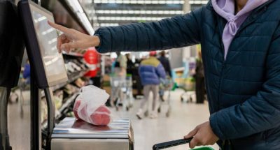 Side view of a man shopping in a supermarket while on a budget. He is weighing the items at the self service checkout in the North East of England. The peppers are in a sustainable mesh bag.