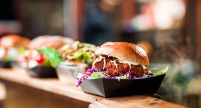 Close up image depicting a burger loaded with crispy fried pork balls on display and for sale at an outdoors food market. The background of the market stall is totally defocused, leaving room for copy space.