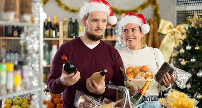 Joyful couple in Santa hats choose products for Christmas dinner. Man and woman with food basket shopping in grocery store