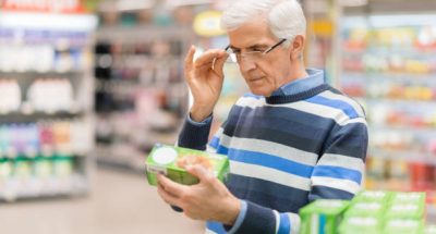 Elderly man shopping in local supermarket. He is holding box and reading nutrition label.