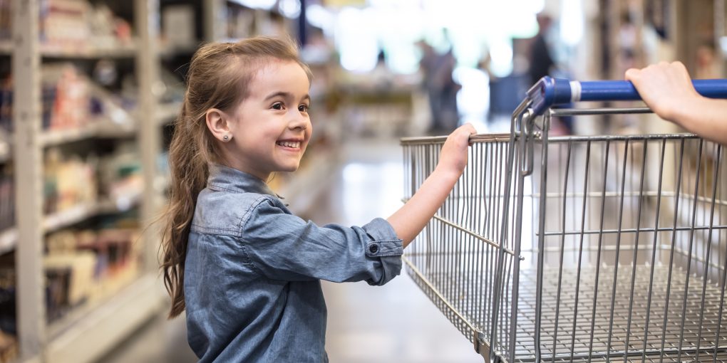 Mother and daughter in blue shirts shopping in supermarket using cart