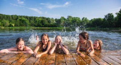 Happy little girls having fun playing in a lake splashing water during summer holidays